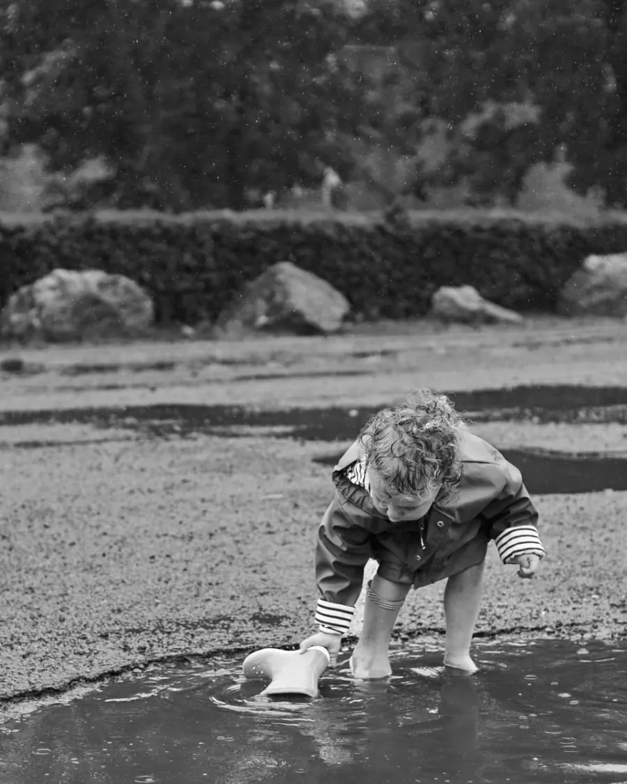 Jeune enfant penché sur une flaque d'eau, en noir et blanc