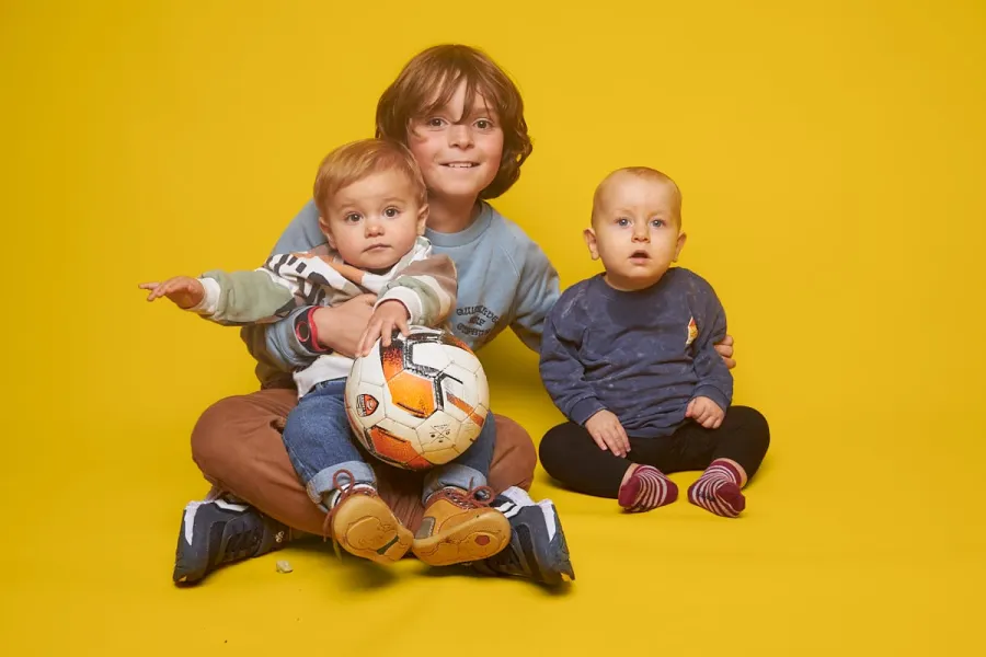 Trois frères assis avec un ballon, sur fond jaune