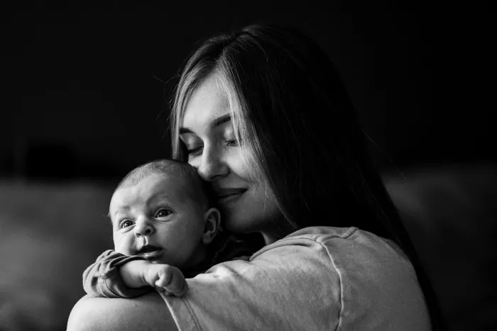 Maman serrant son nouveau-né contre sa joue, en noir et blanc