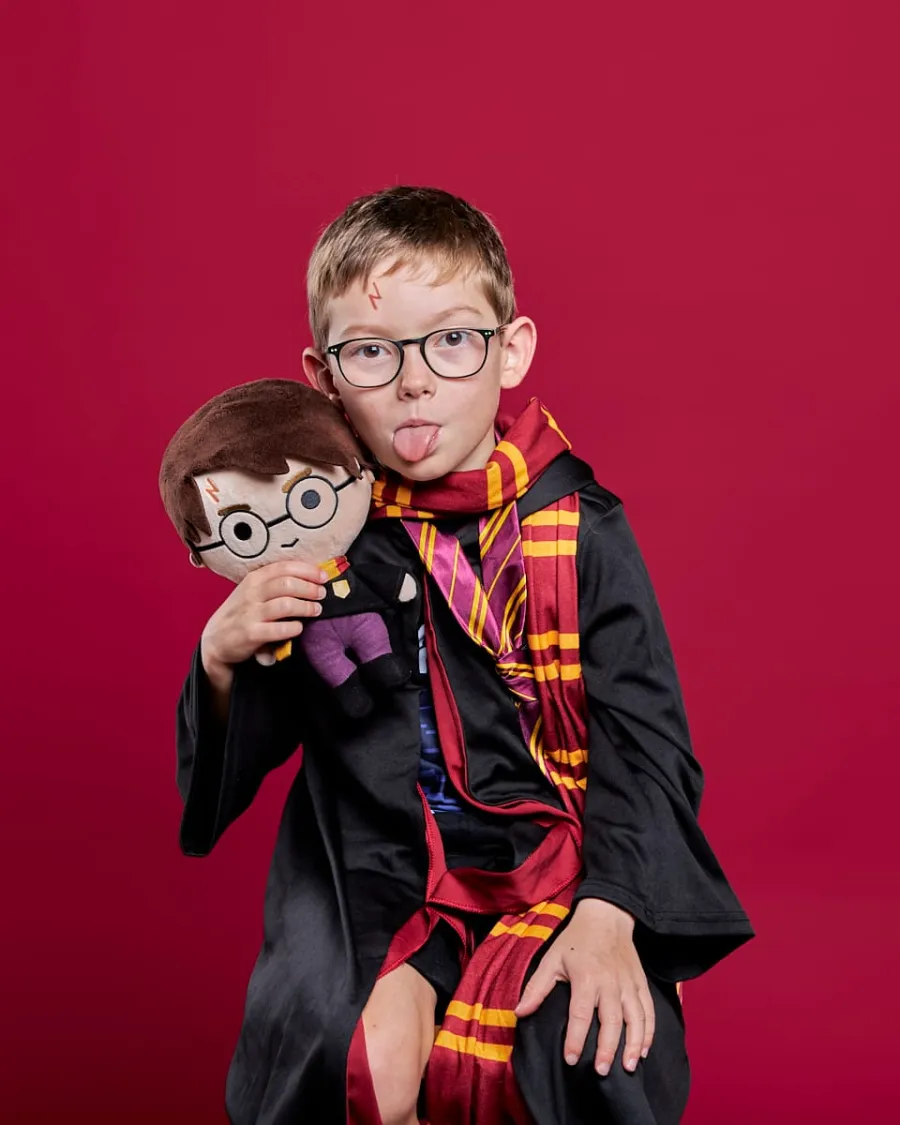 Garçon à lunettes déguisé en sorcier, tirant la langue avec sa peluche, sur fond rouge