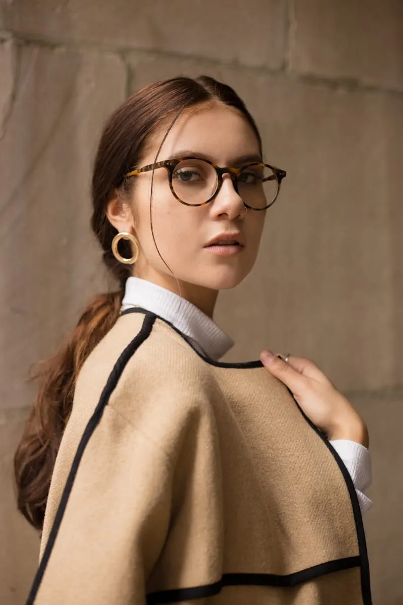 Portrait d'une femme à lunettes en manteau beige, contre un mur de pierre
