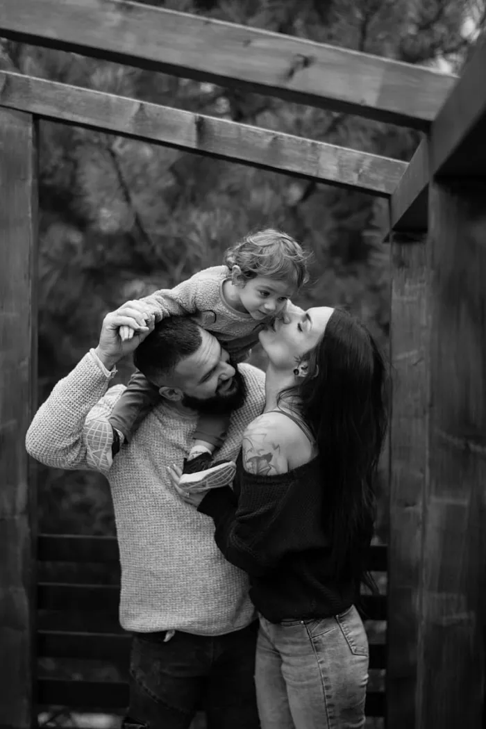 Famille en extérieur, l'enfant juché sur les épaules de son papa, en noir et blanc