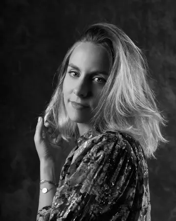 Femme aux cheveux blonds mi-longs regardant par-dessus l’épaule, la main dans les cheveux, en noir et blanc